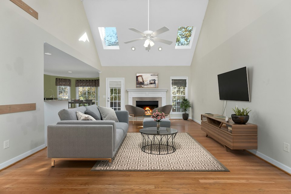 Family room with a vaulted ceiling, skylights, a ceiling fan, a gray sofa and a fireplace