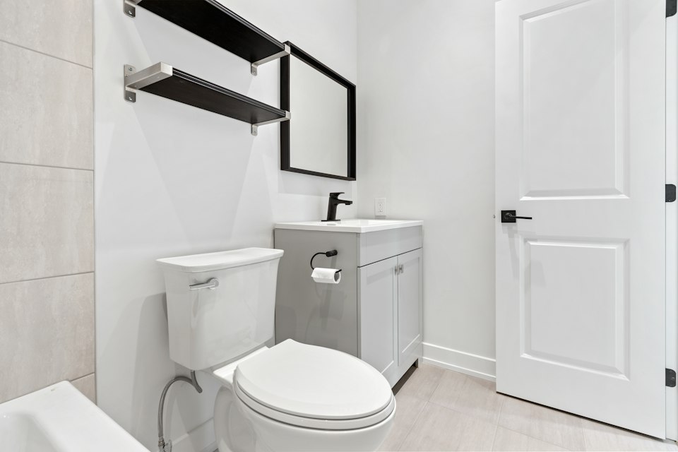 Half bath with a toilet, a gray vanity, a black-framed mirror and open shelves