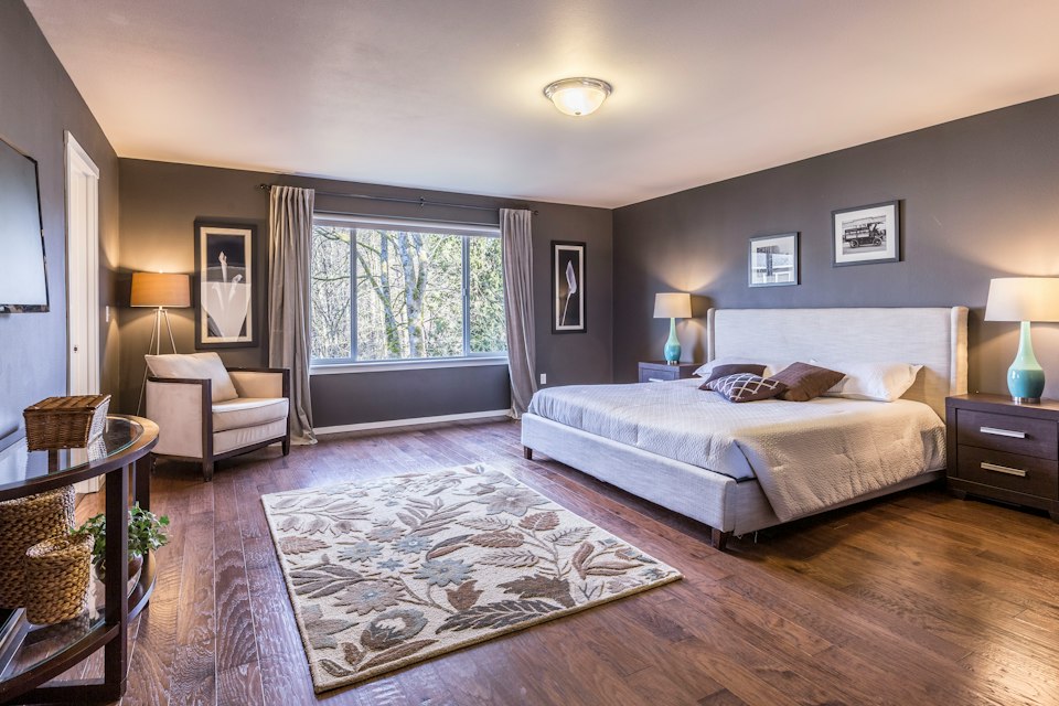 Large bedroom with gray walls, a king-size bed, a patterned area rug, wood floors and a wide window